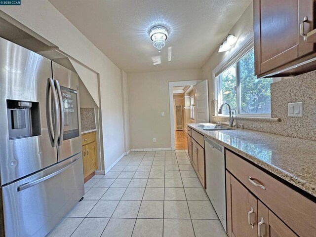 kitchen with sink, light stone counters, light tile patterned floors, stainless steel appliances, and backsplash