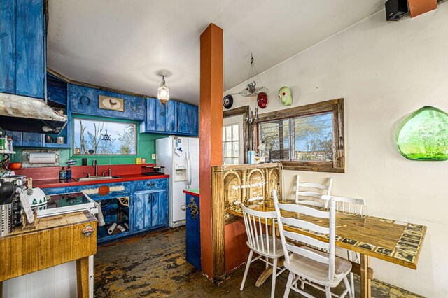 kitchen featuring white refrigerator with ice dispenser, sink, lofted ceiling, and blue cabinetry