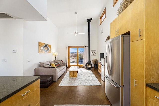 kitchen featuring a towering ceiling, a wood stove, ceiling fan, and stainless steel fridge with ice dispenser