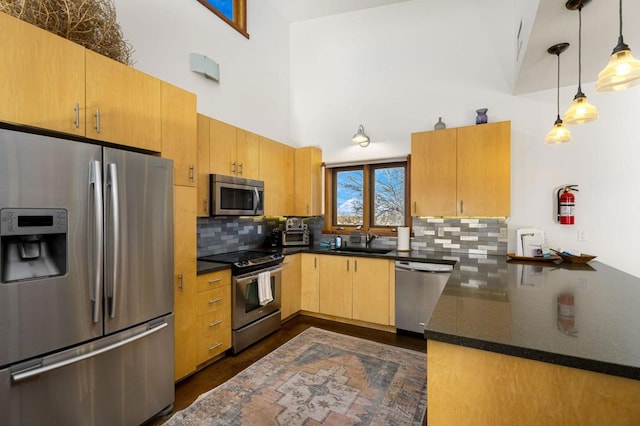 kitchen featuring sink, hanging light fixtures, a towering ceiling, stainless steel appliances, and decorative backsplash