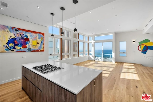 kitchen with a water view, stainless steel gas cooktop, light wood-type flooring, and decorative light fixtures