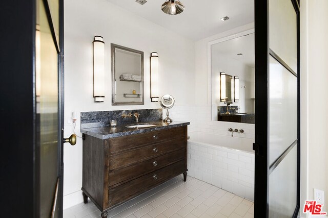 bathroom featuring a relaxing tiled tub, vanity, and tile patterned flooring