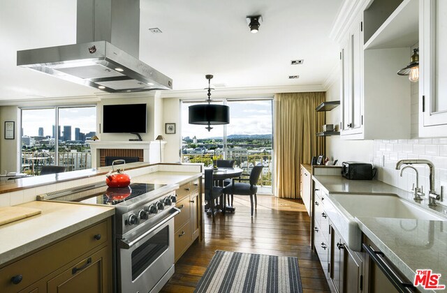 kitchen with white cabinets, a wealth of natural light, island exhaust hood, high end stove, and backsplash