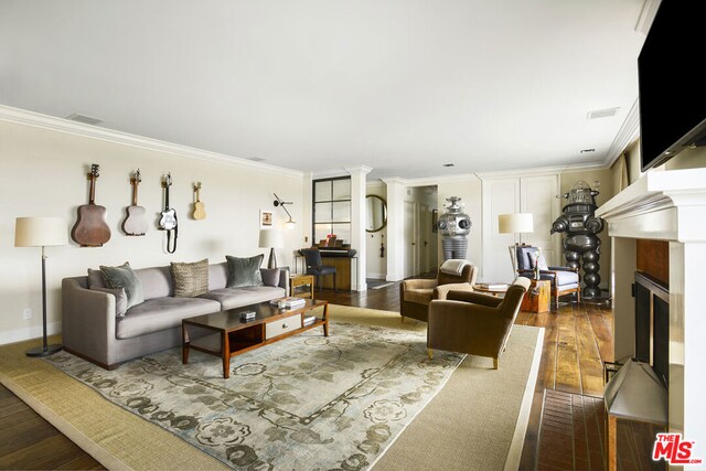 living room featuring dark hardwood / wood-style flooring, crown molding, and decorative columns