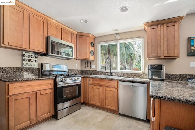 kitchen with stainless steel appliances, sink, and dark stone counters