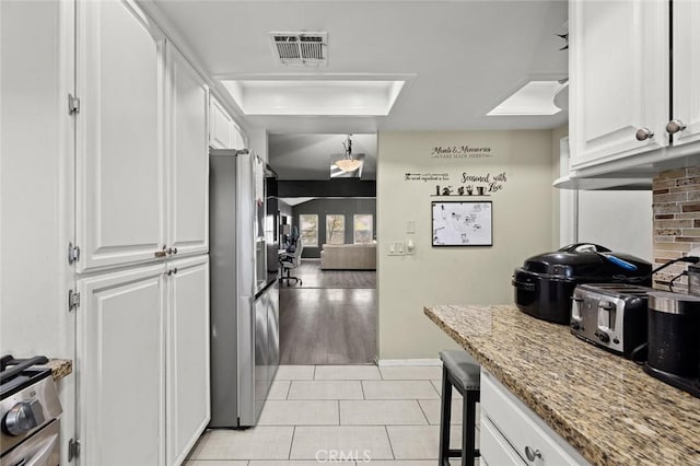 kitchen with white cabinetry, stainless steel appliances, light stone counters, and light tile patterned floors