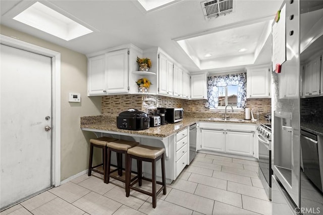 kitchen featuring stone counters, white cabinetry, stainless steel appliances, a tray ceiling, and kitchen peninsula