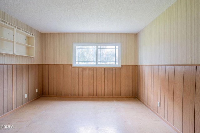 spare room featuring built in shelves, a textured ceiling, and wood walls