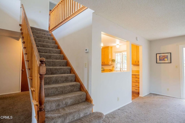 stairs featuring carpet, sink, and a textured ceiling