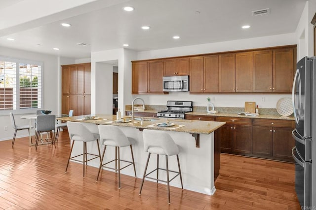 kitchen featuring a breakfast bar, sink, light wood-type flooring, stainless steel appliances, and a kitchen island with sink