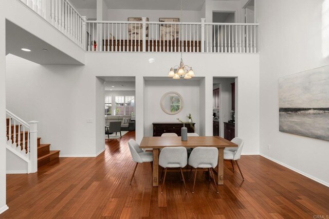 dining area with hardwood / wood-style flooring, a towering ceiling, and a chandelier