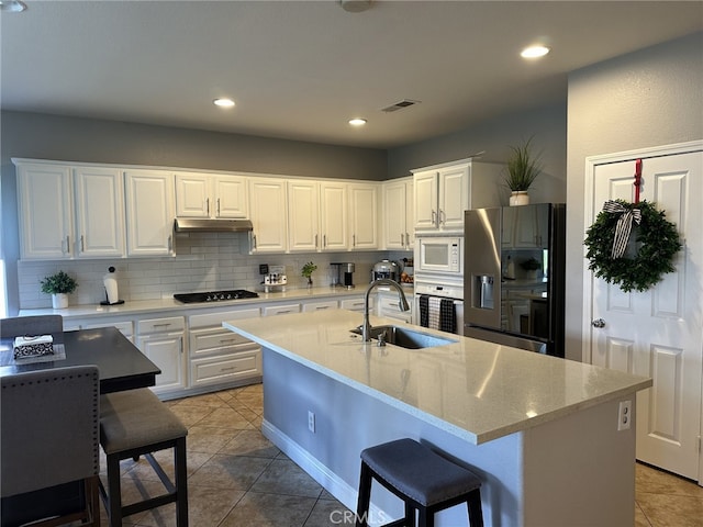 kitchen with sink, white cabinets, decorative backsplash, a kitchen island with sink, and white appliances