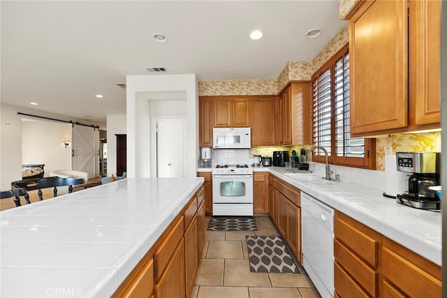 kitchen featuring tile countertops, sink, decorative backsplash, a barn door, and white appliances