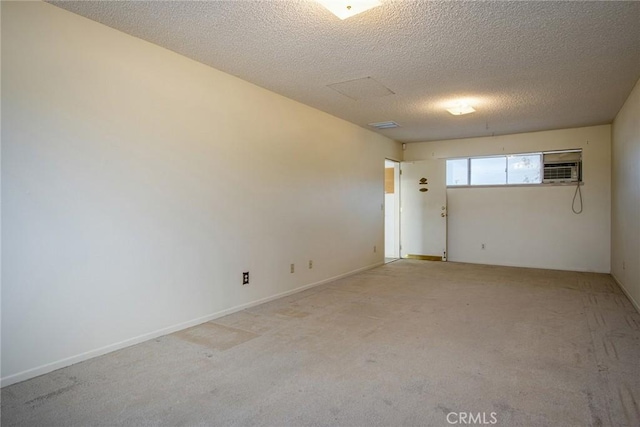 empty room featuring light colored carpet, a wall mounted AC, and a textured ceiling