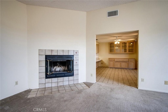 unfurnished living room featuring light carpet, a tiled fireplace, and a textured ceiling