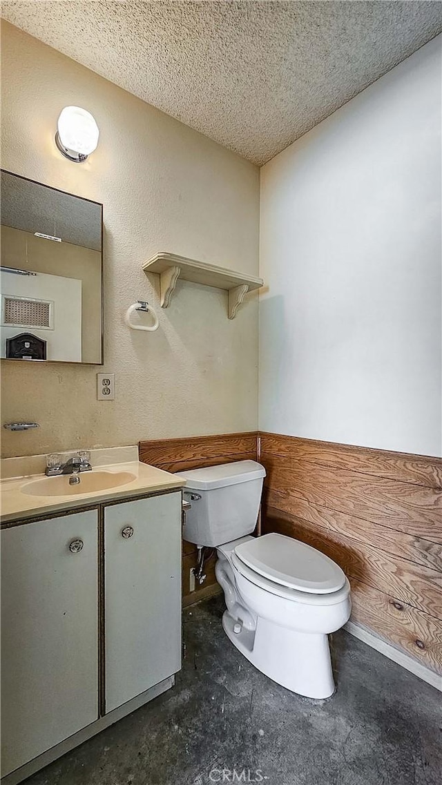 bathroom with vanity, a textured ceiling, concrete flooring, and toilet