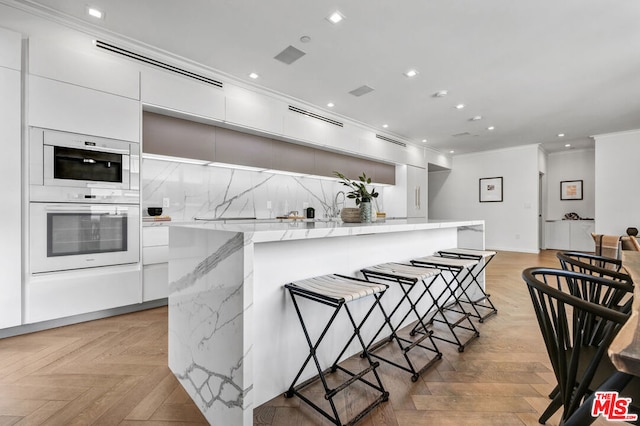 kitchen with ornamental molding, a kitchen breakfast bar, decorative backsplash, and white cabinets