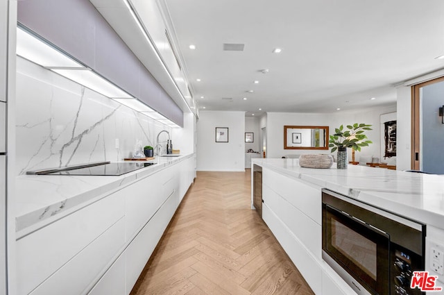 kitchen with sink, light stone counters, black appliances, light parquet floors, and white cabinets