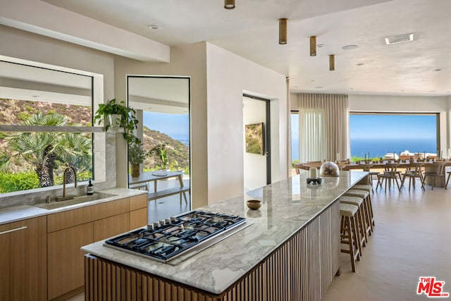 kitchen featuring sink, a kitchen bar, a center island, stainless steel gas cooktop, and a water view