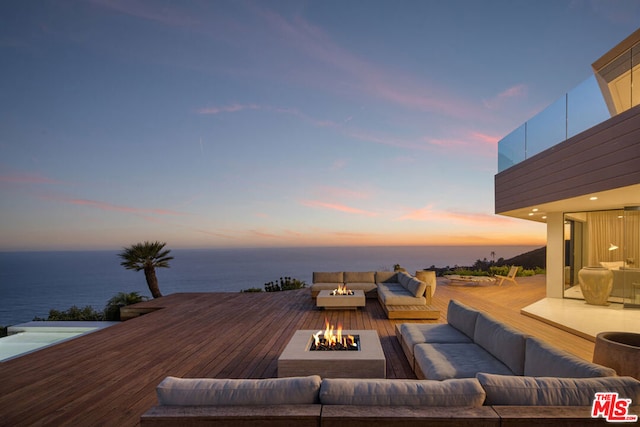 deck at dusk with an outdoor living space with a fire pit and a water view