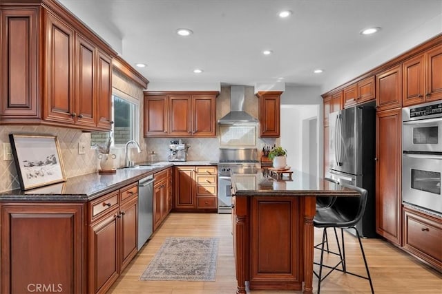 kitchen featuring stainless steel appliances, light hardwood / wood-style floors, a kitchen island, dark stone counters, and wall chimney exhaust hood