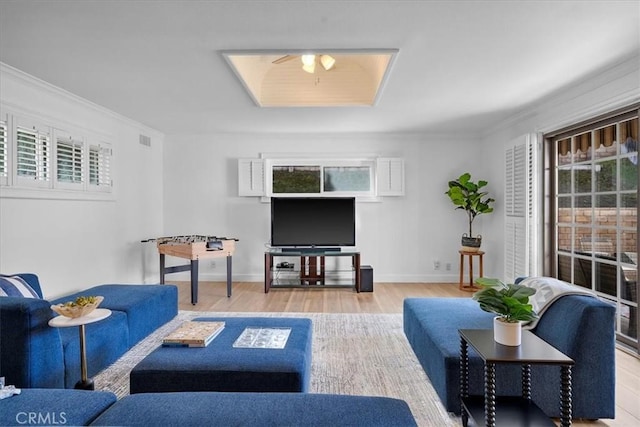 living room with a wealth of natural light, ornamental molding, and light wood-type flooring