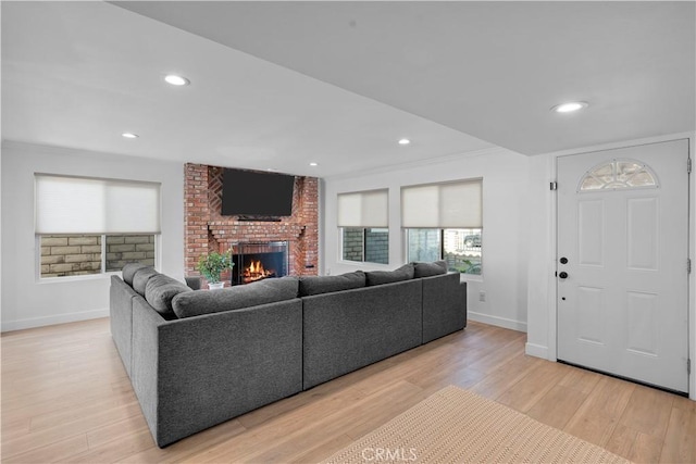 living room with ornamental molding, a brick fireplace, and light hardwood / wood-style flooring