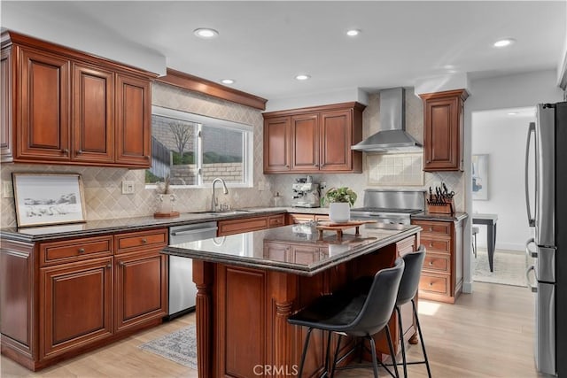 kitchen featuring wall chimney range hood, sink, appliances with stainless steel finishes, a center island, and dark stone counters