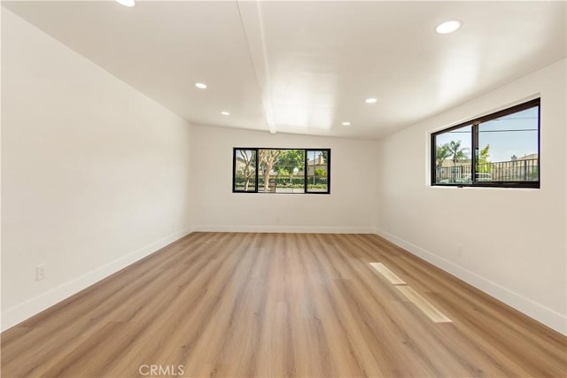 empty room featuring beamed ceiling, light hardwood / wood-style flooring, and a wealth of natural light