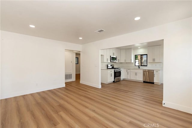 kitchen with appliances with stainless steel finishes, sink, light wood-type flooring, and white cabinets