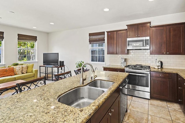 kitchen with stainless steel appliances, light stone countertops, sink, and backsplash