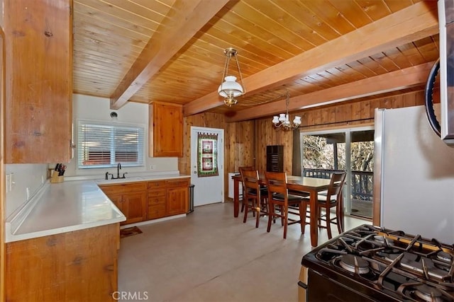 kitchen featuring range with gas stovetop, wood walls, sink, stainless steel fridge, and hanging light fixtures