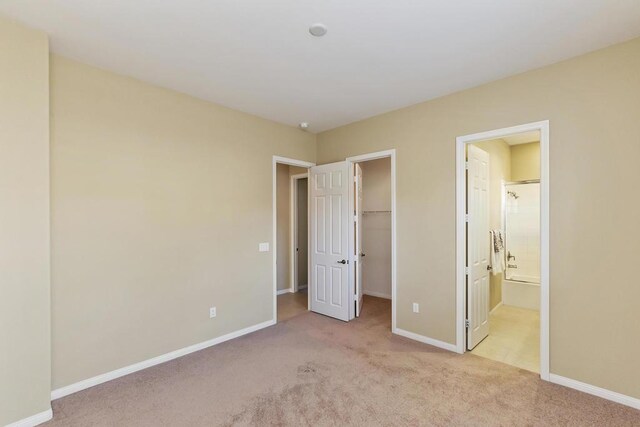 unfurnished bedroom with ensuite bathroom, a spacious closet, light carpet, and a closet