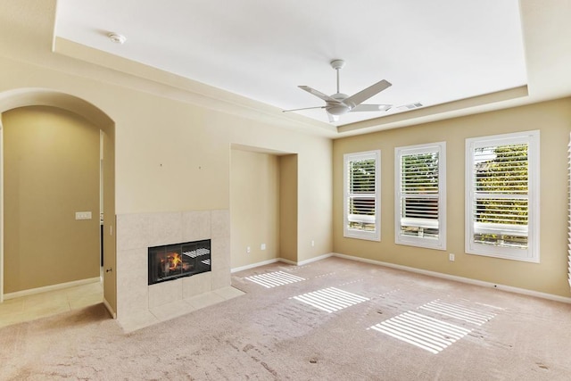 unfurnished living room with a fireplace, light colored carpet, a raised ceiling, and ceiling fan