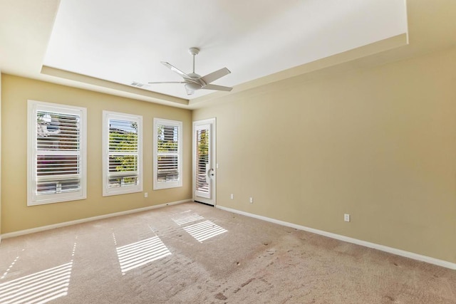 carpeted spare room with a tray ceiling and ceiling fan