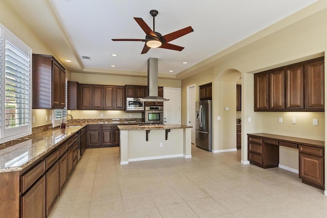 kitchen featuring light stone counters, built in desk, a kitchen island, island exhaust hood, and stainless steel appliances