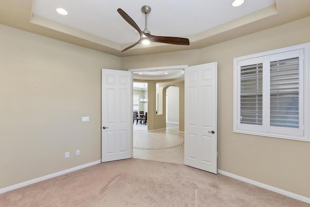 carpeted spare room featuring ceiling fan and a raised ceiling