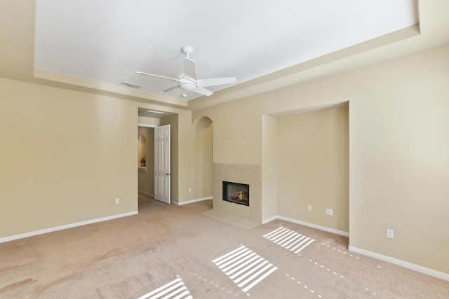 unfurnished living room featuring a raised ceiling, ceiling fan, light colored carpet, and a fireplace