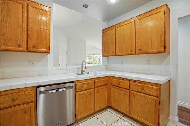 kitchen with light tile patterned flooring, sink, stainless steel dishwasher, and tile counters