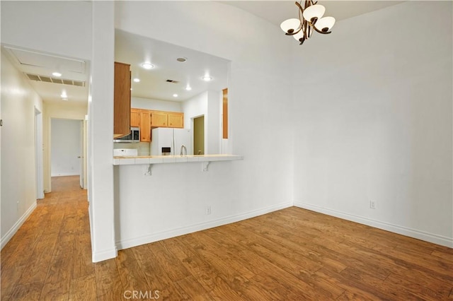 kitchen with an inviting chandelier, a kitchen breakfast bar, kitchen peninsula, white refrigerator with ice dispenser, and light hardwood / wood-style floors