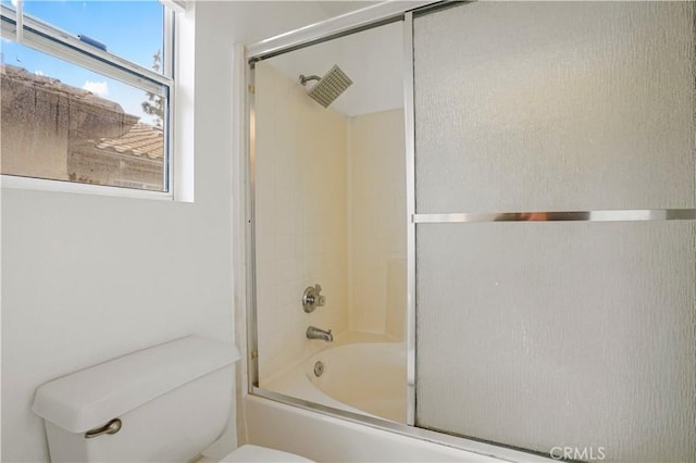 bathroom with toilet and shower / bath combination with glass door