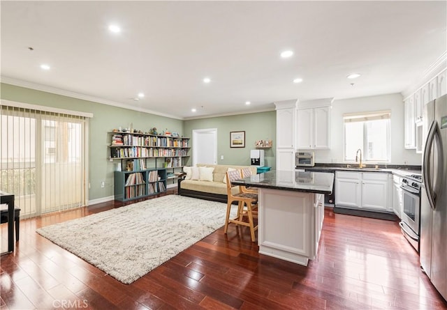 kitchen with sink, gas stove, dark stone countertops, a kitchen island, and white cabinets