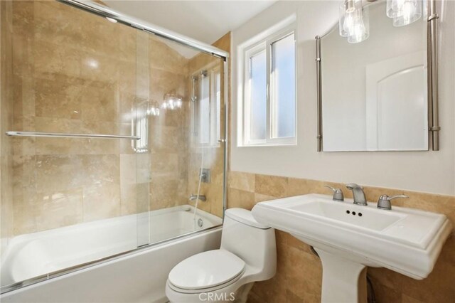 full bathroom with sink, toilet, combined bath / shower with glass door, and tile walls