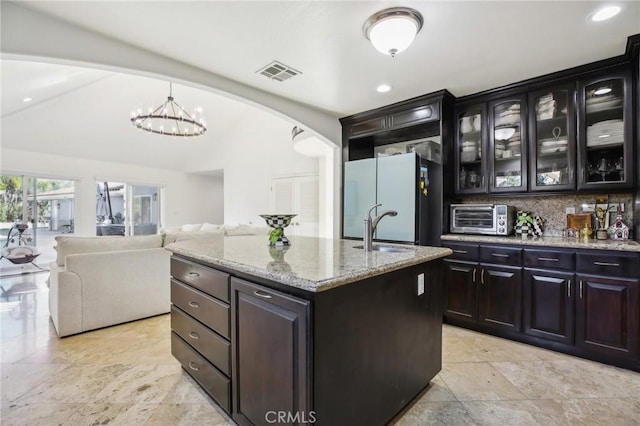 kitchen with sink, hanging light fixtures, backsplash, white refrigerator, and an island with sink