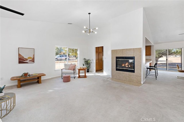 carpeted living room featuring an inviting chandelier, high vaulted ceiling, and a tile fireplace