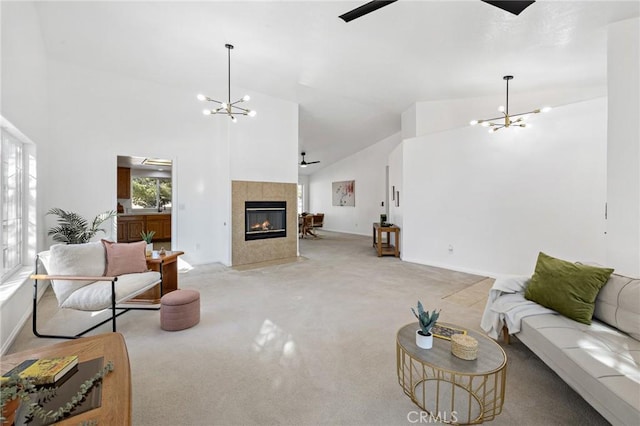 living room featuring high vaulted ceiling, ceiling fan with notable chandelier, light colored carpet, and a tile fireplace