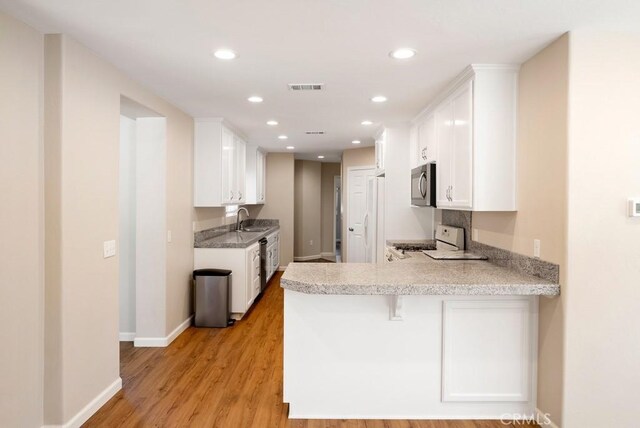 kitchen with appliances with stainless steel finishes, white cabinetry, sink, kitchen peninsula, and light hardwood / wood-style flooring