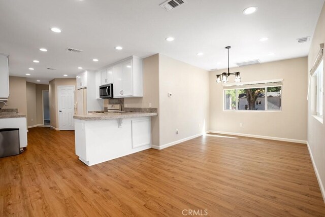 kitchen with a kitchen bar, light wood-type flooring, kitchen peninsula, white fridge with ice dispenser, and white cabinets