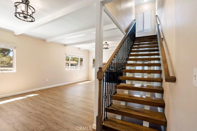 stairway with beamed ceiling, wood-type flooring, and a notable chandelier