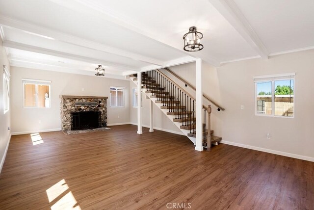 unfurnished living room with beamed ceiling, dark hardwood / wood-style flooring, an inviting chandelier, and a stone fireplace